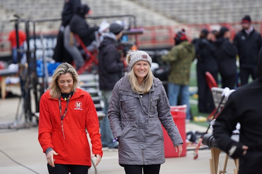 A stylish woman bundled in a cozy coat watching a youth sports game outdoors.