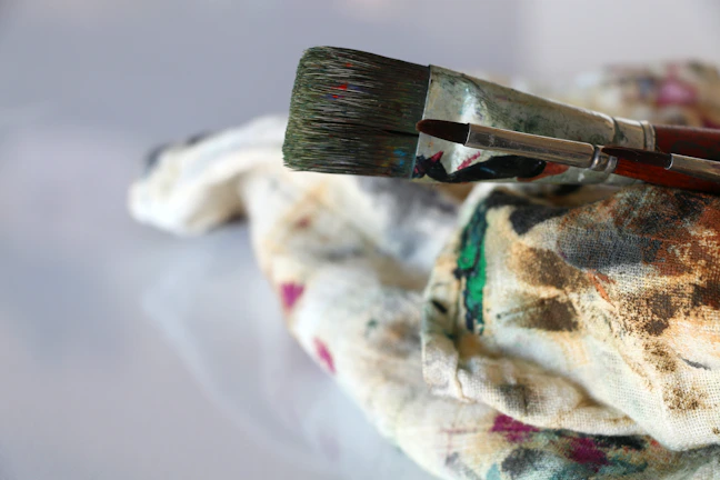 Brushes and rollers resting on a drop cloth, with fresh paint strokes visible on a wooden surface.