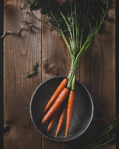 Fresh carrots and tomatoes displayed in a rustic wooden crate on a farm table.