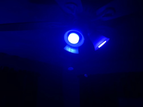 A ceiling fan with multiple light fixtures, all emitting a bright blue light, casting an intense glow over the dark surroundings.