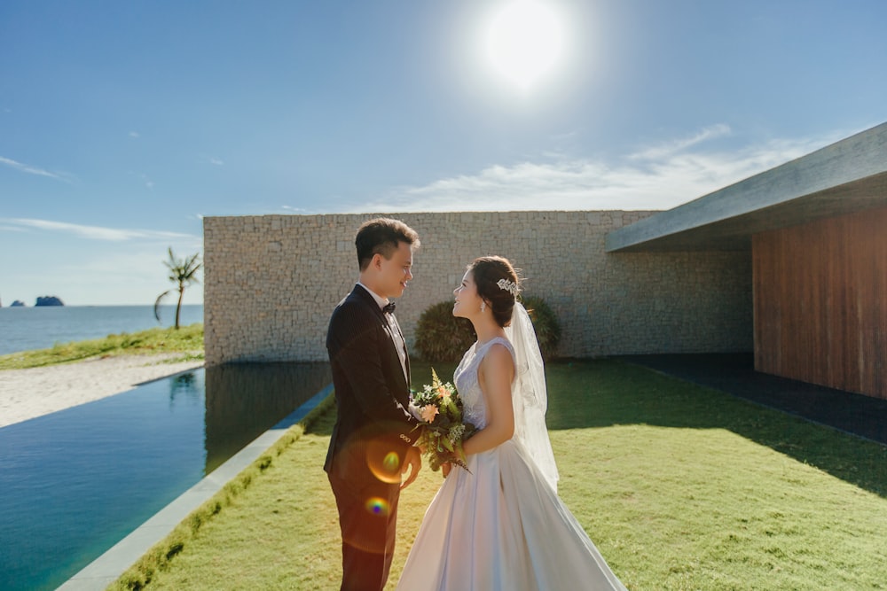 man and woman wearing wedding dresses standing beside body of water