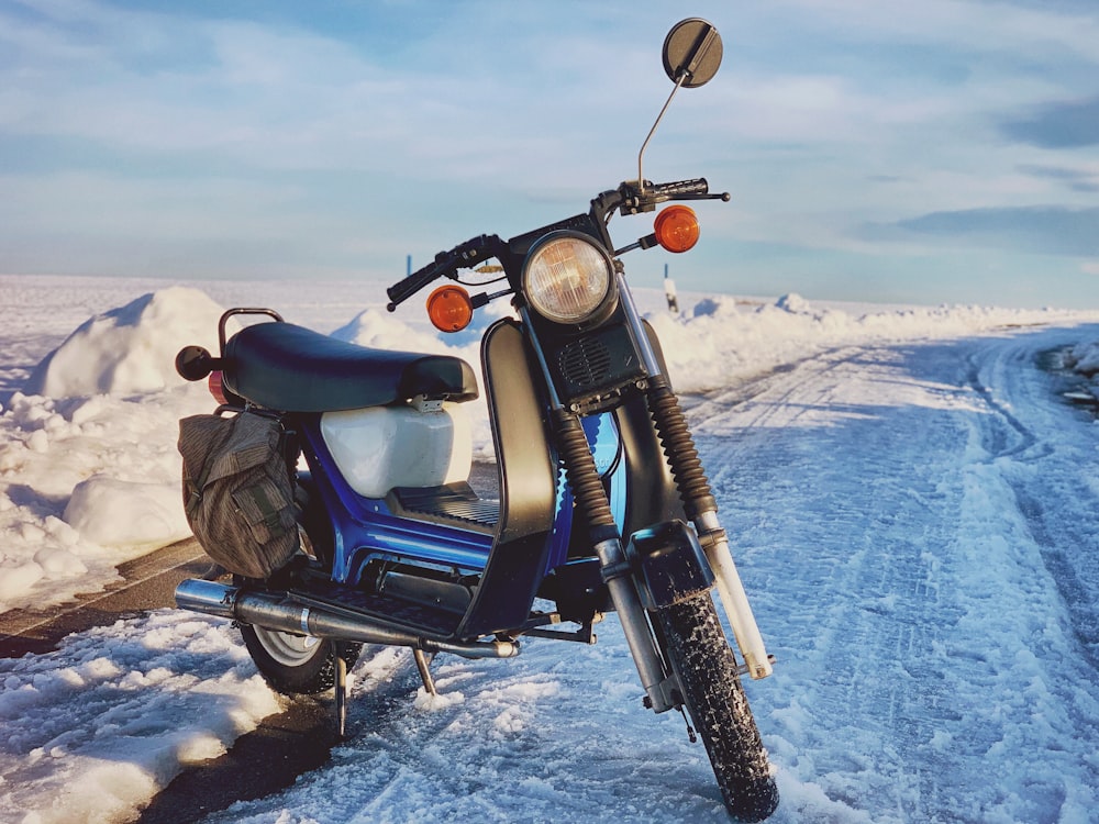 Moto noire et bleue garée sur une route enneigée pendant la journée