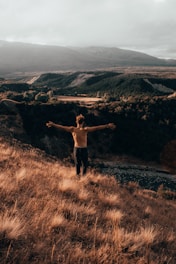 man raising two hands standing in front of body of water during daytime