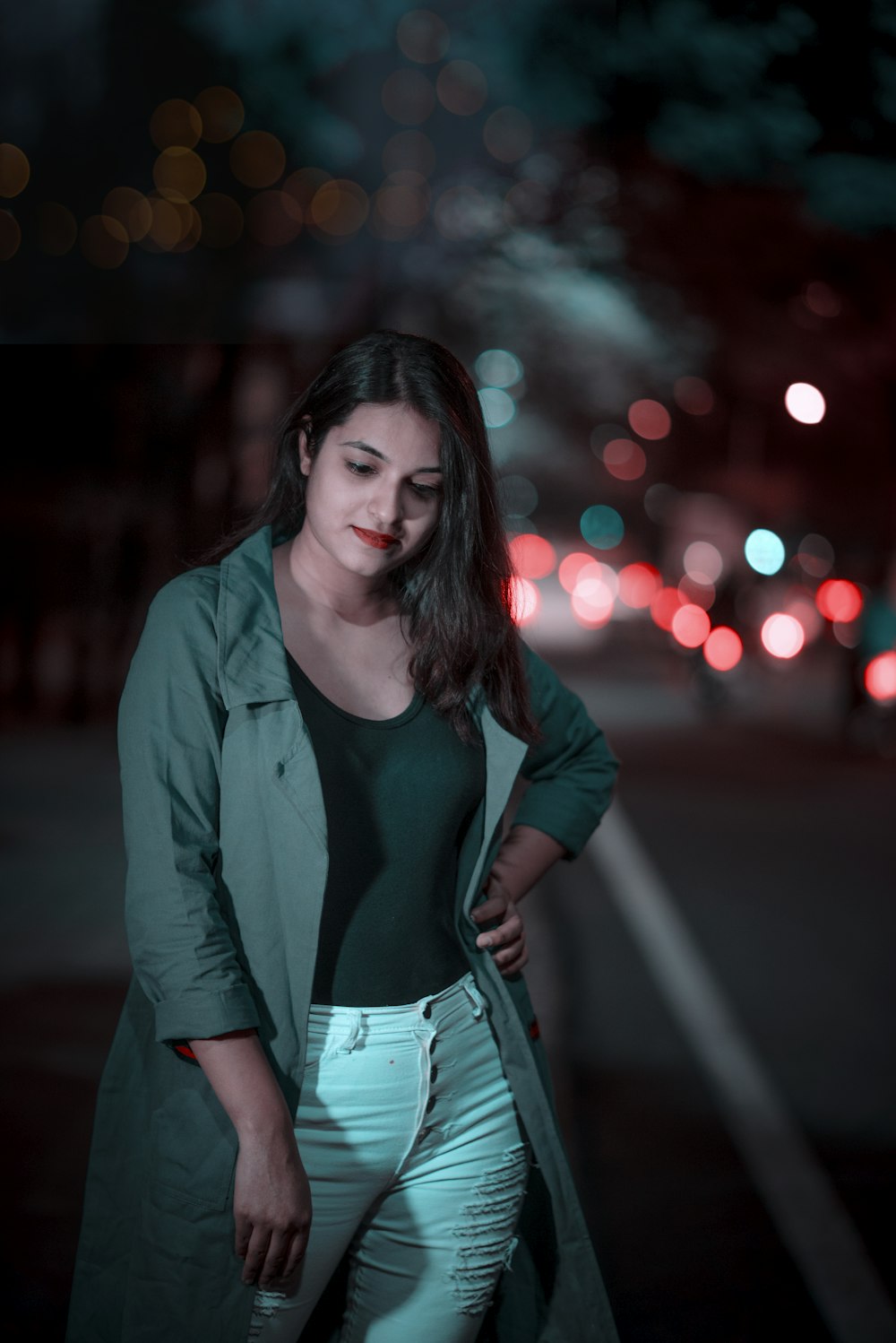 woman in black scoop-neck top, gray coat, and white jeans standing on sidewalk