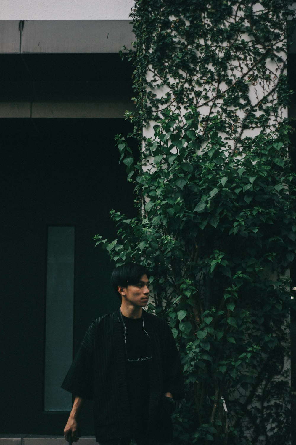 man standing beside wall covered with plants