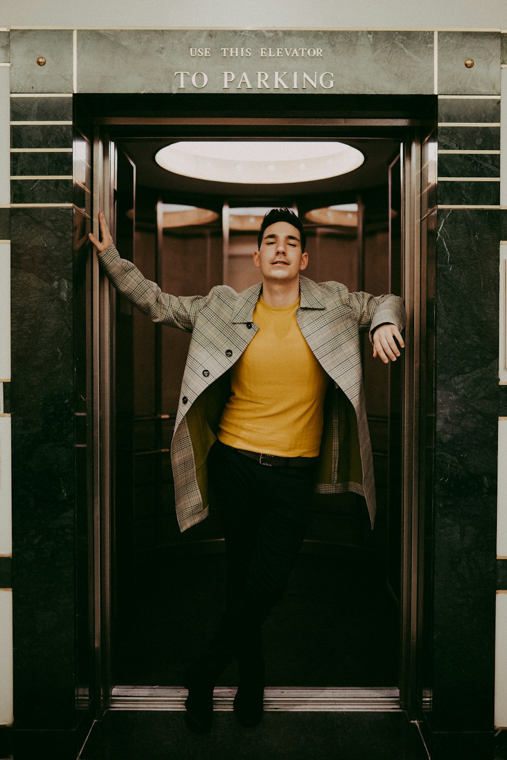 man in yellow shirt and gray coat leaning hands outside elevator