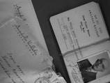 Several documents and an envelope are displayed, including a membership card with printed text and a black-and-white photograph of an older man wearing glasses. The envelope has handwritten addresses and a few stamps attached.