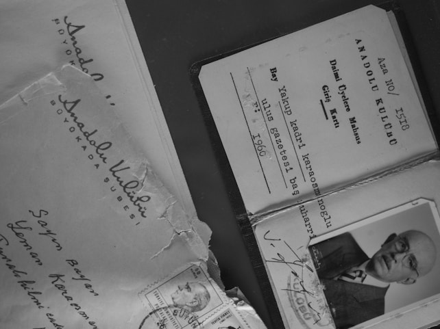 Several documents and an envelope are displayed, including a membership card with printed text and a black-and-white photograph of an older man wearing glasses. The envelope has handwritten addresses and a few stamps attached.