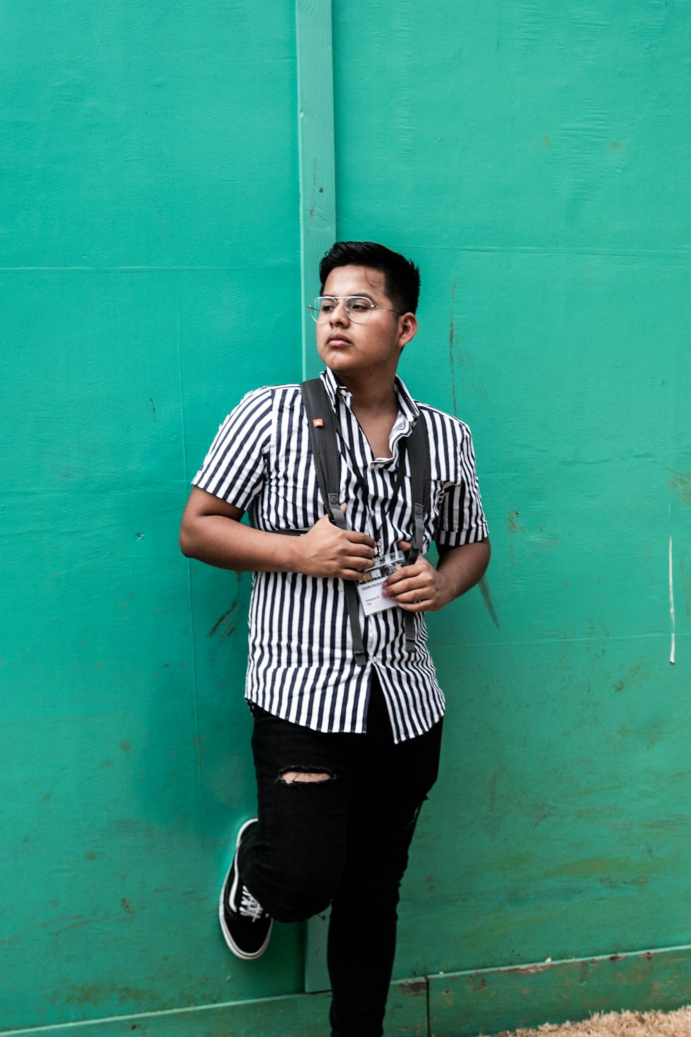 man wearing black and white stripe dress shirt leaning on green wall