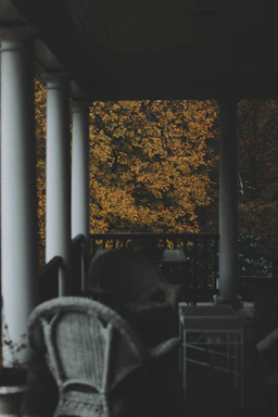 Inviting front porch of a classic New Hampshire farmhouse surrounded by autumn foliage.
