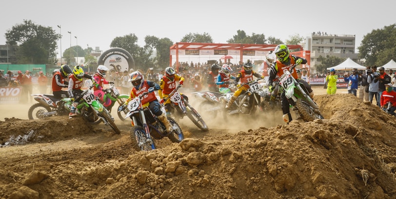 Riders launching off a dirt ramp during a sunny motocross race at sõmerpalu track