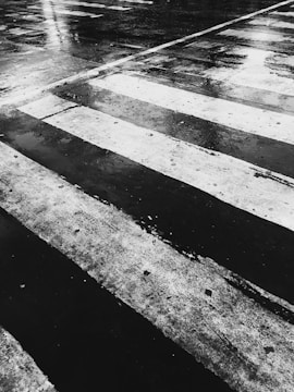 A wet, reflective road surface with a visible crosswalk pattern of white lines set against dark asphalt.