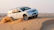 A shiny white SUV cruising along a desert road with golden dunes in the background.