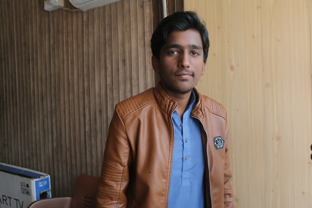 man wearing brown leather jacket leaning on wooden wall