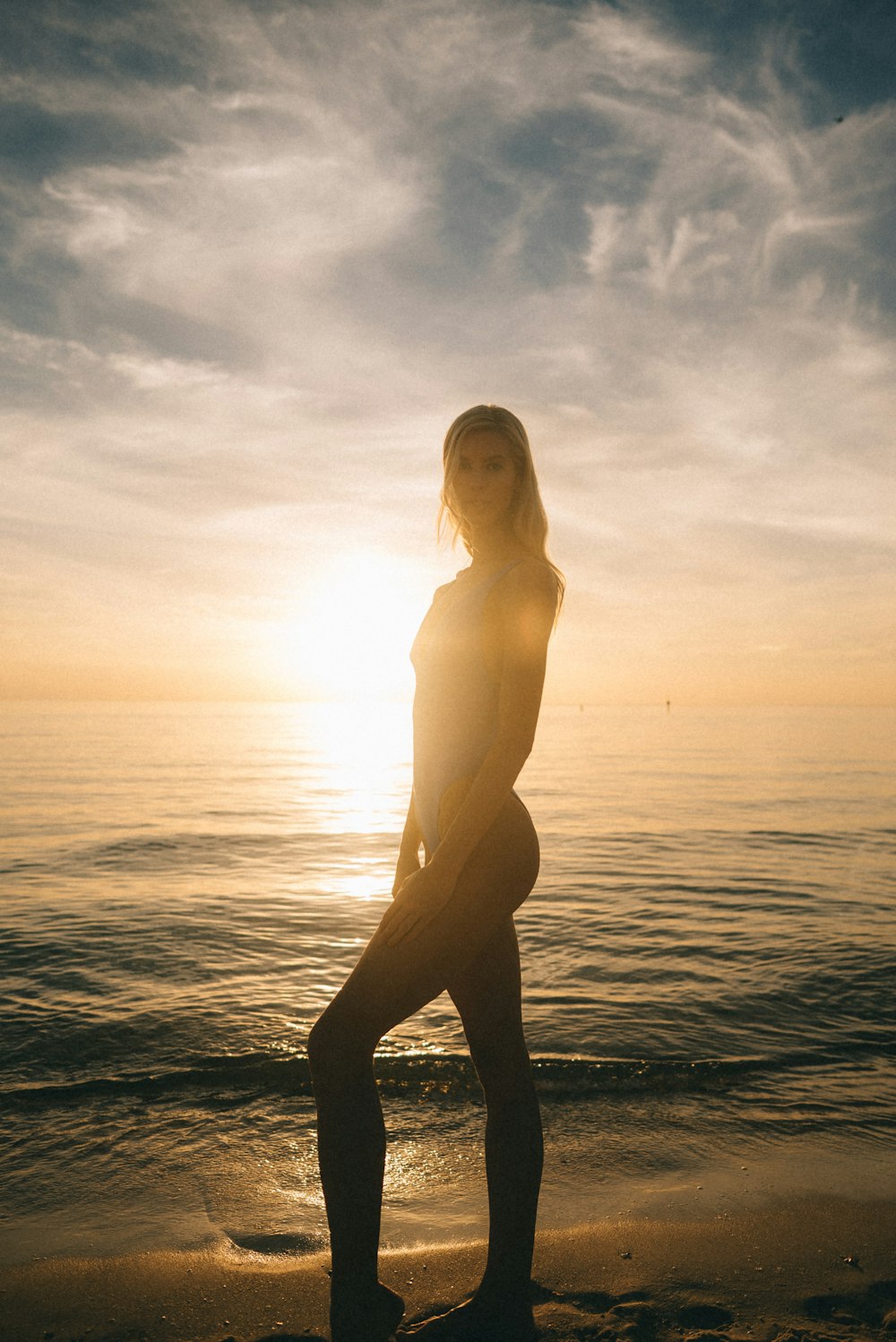 Frau im Badeanzug posiert bei Sonnenuntergang am Strand