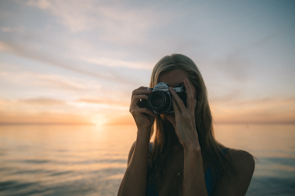 woman wearing blue top holding gray DSLR camera