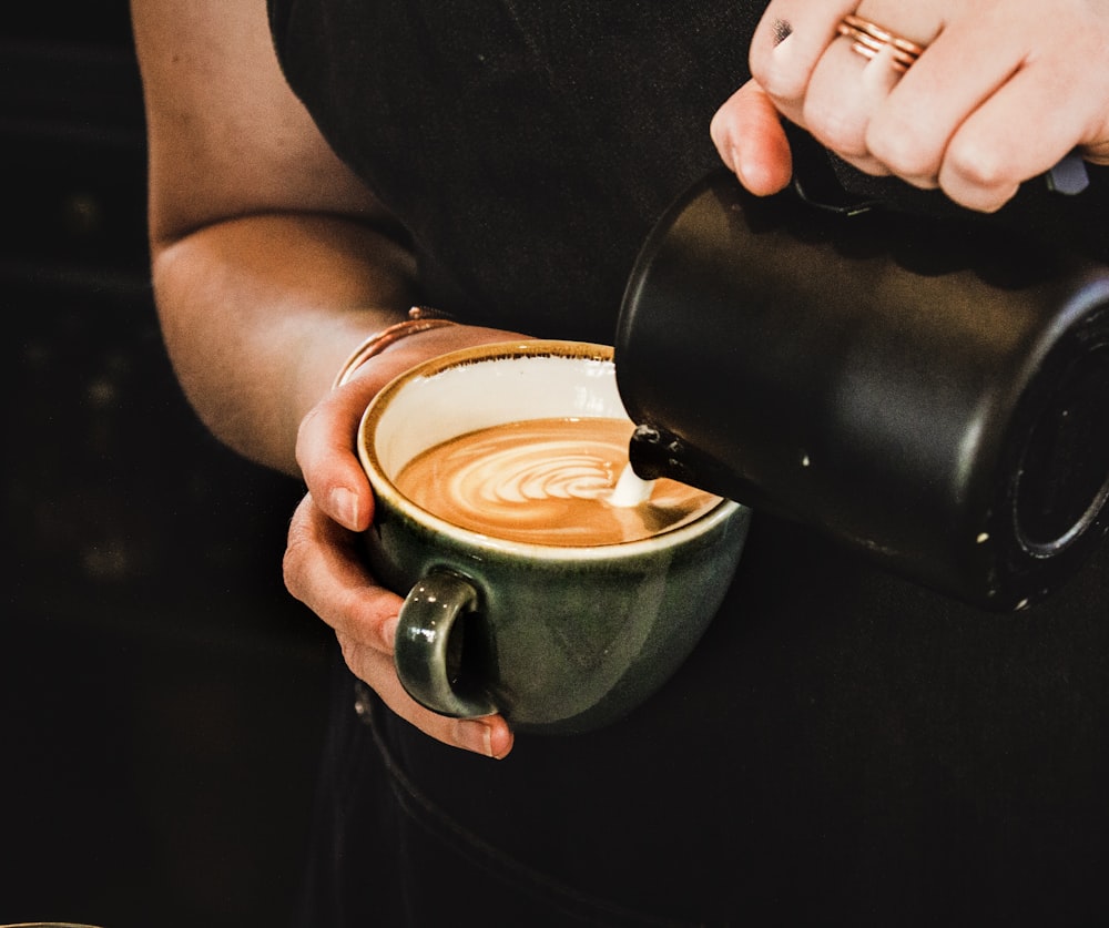 person pouring cappuccino on gray mug