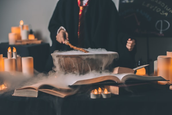 Wizard with a wand over a cauldron and open books. 