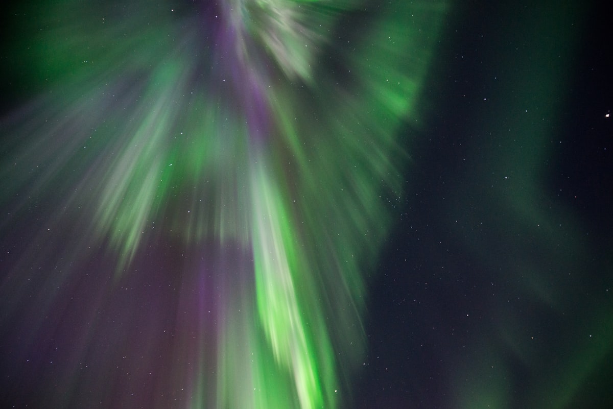 Green northern lights over a snow-covered forest and frozen lake in Finnish Lapland on a clear winter night