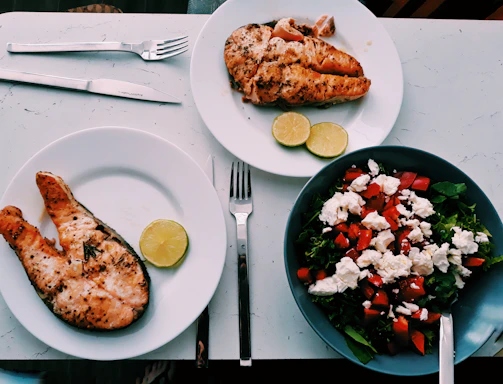 An elegant table setting showcasing plated grilled salmon and fresh Caesar salad with gold and black accents.