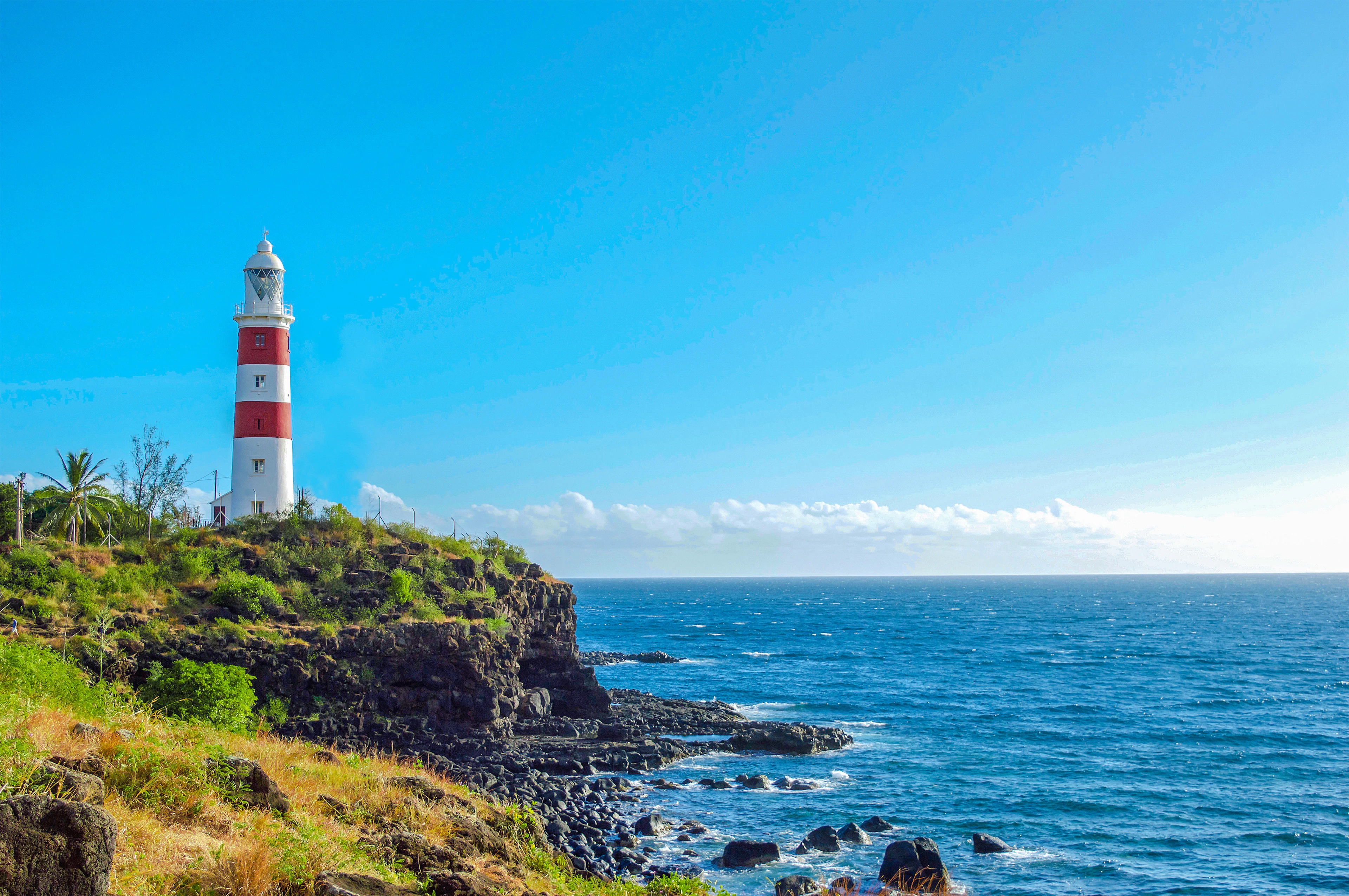 A red-and-white striped lighthouse stands on a rocky volcanic point above a turquoise sea.