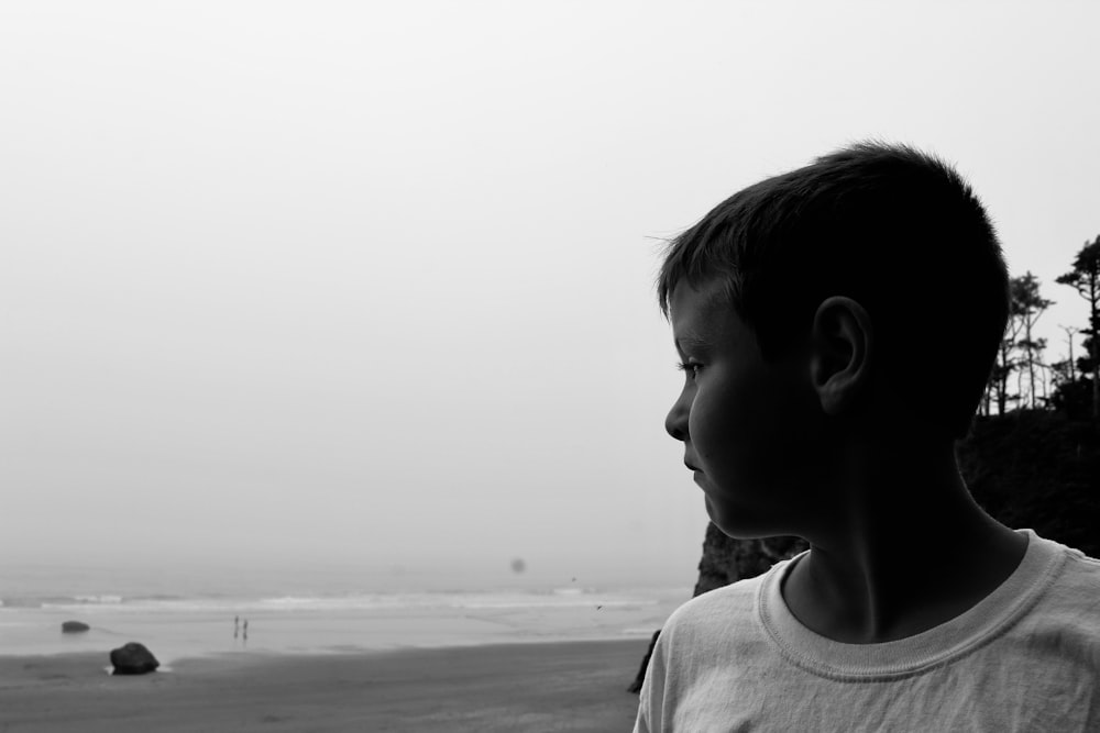 Photographie en niveaux de gris d’un garçon près du bord de mer