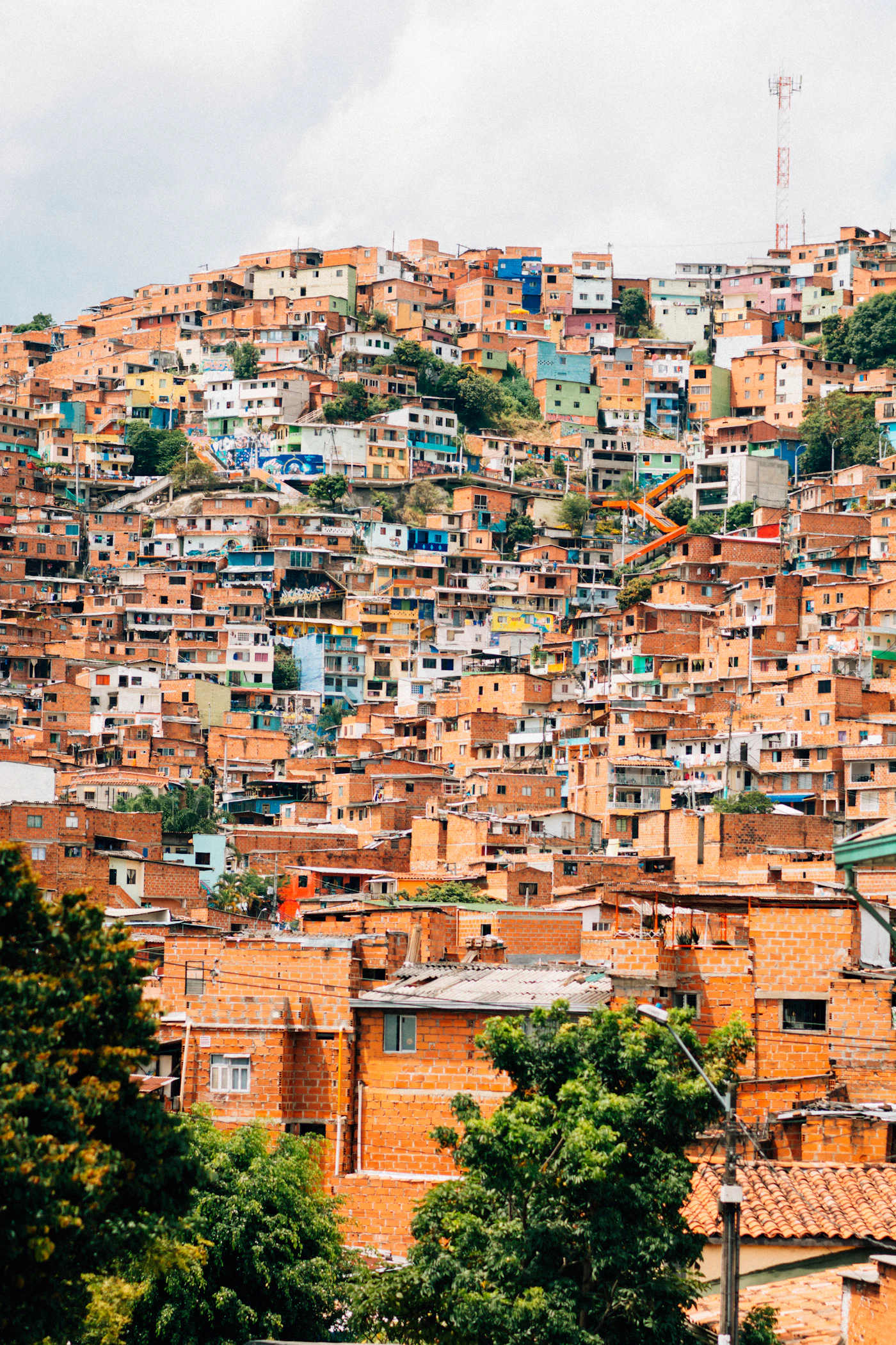 Dense hillside barrio in Medell&iacute;n Colombia with rows of orange-brick buildings climbing steeply up the Andes mountainside above the city