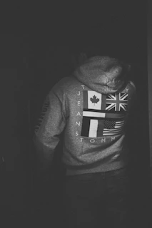 A rugged man wearing a black hoodie with a sharp, edgy American flag design in red and aged white.