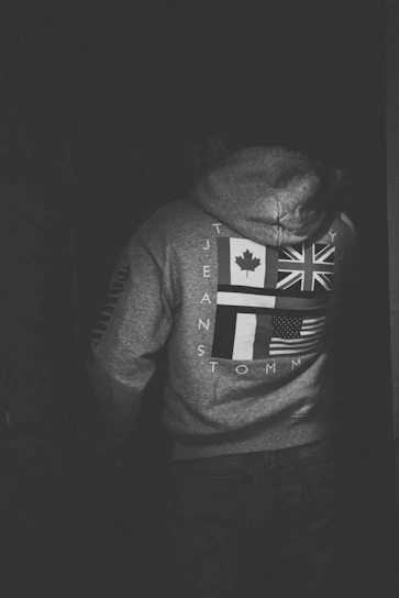 A rugged man wearing a black hoodie with a sharp, edgy American flag design in red and aged white.