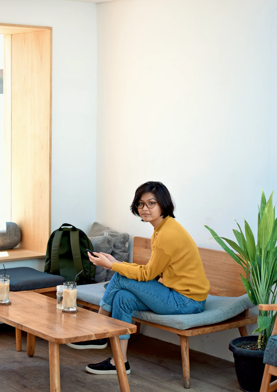 Perempuan berkacamata duduk santai di kamar dengan ransel