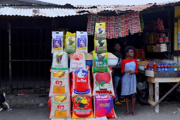 A neatly arranged display of daily staple products including rice, sugar, cooking oil, and flour on a wooden table.