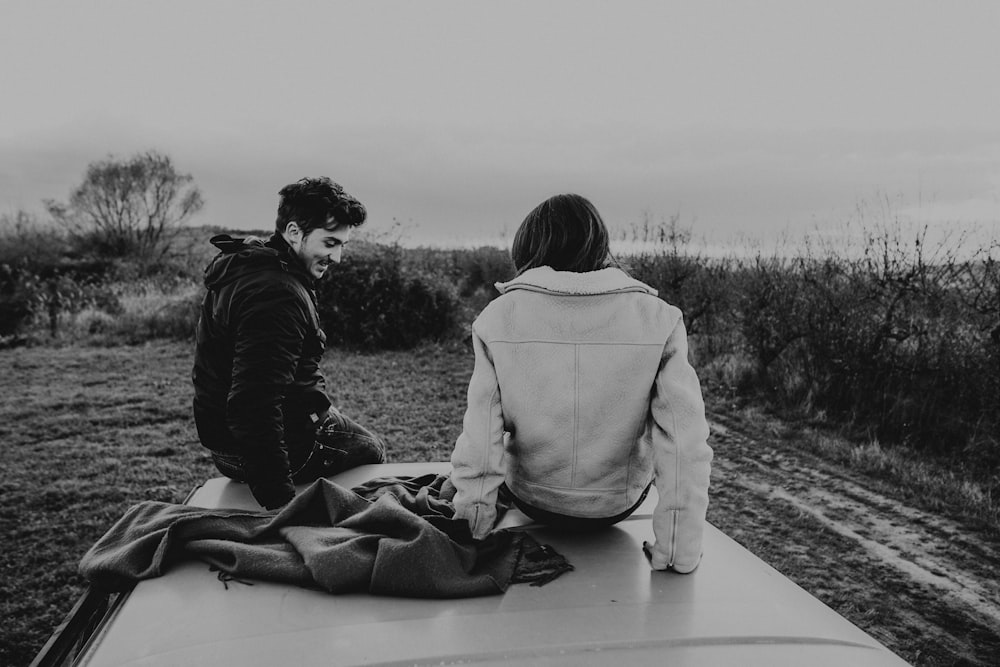 grayscale photography of woman and man sitting on top of vehicle