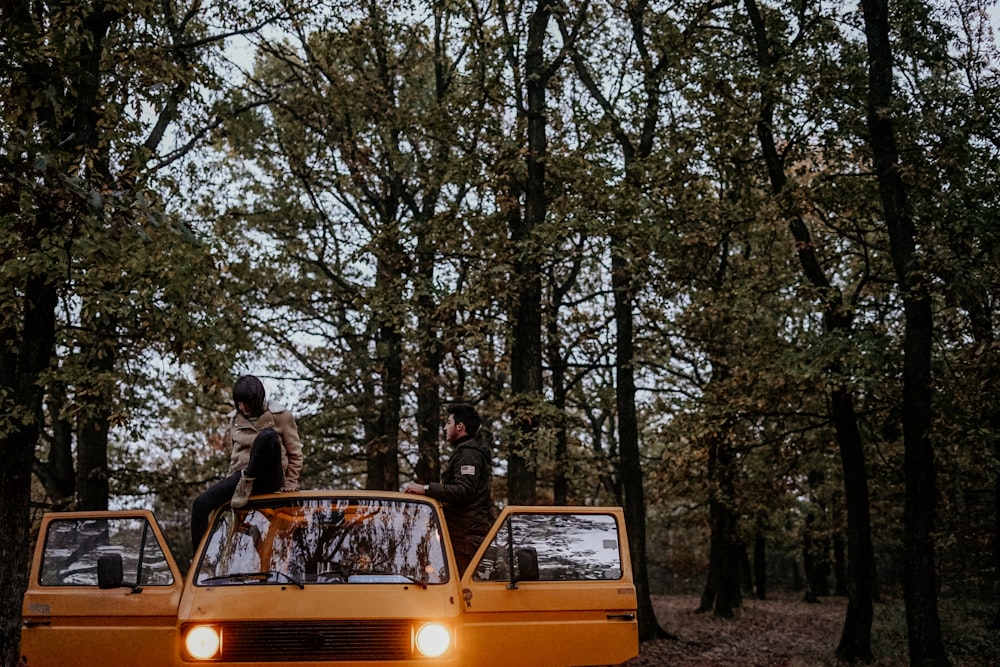 Zwei Männer fahren tagsüber auf einem gelben Lieferwagen im Wald