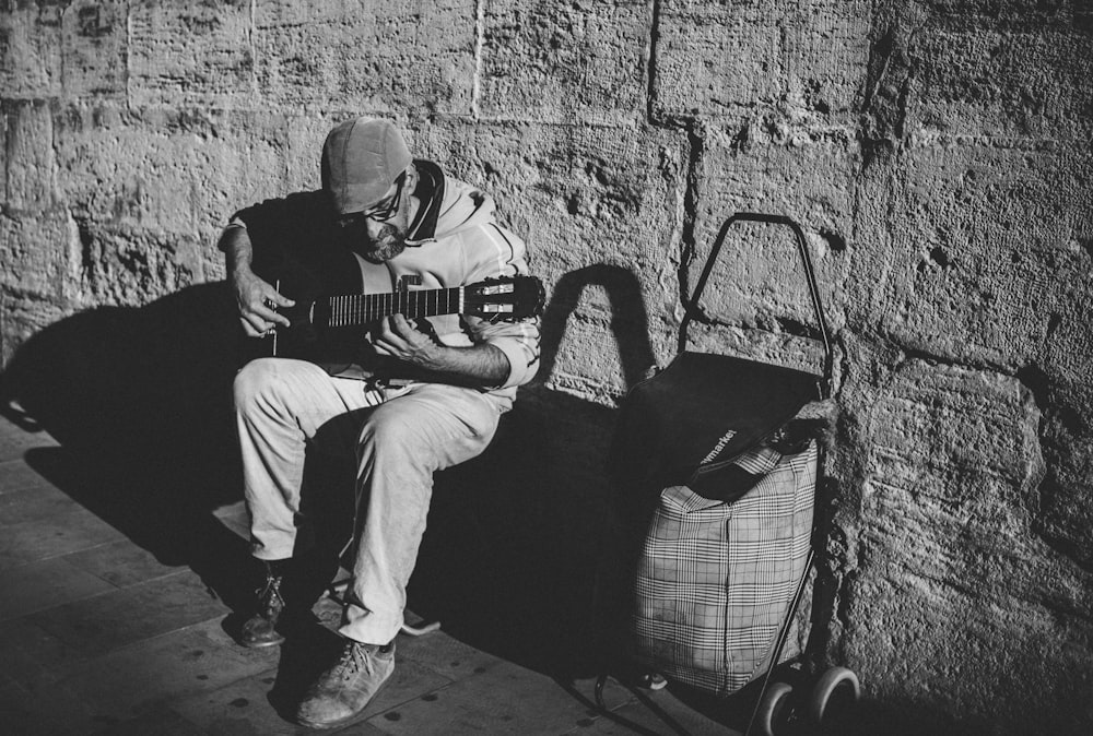 man sitting and playing guitar near wall