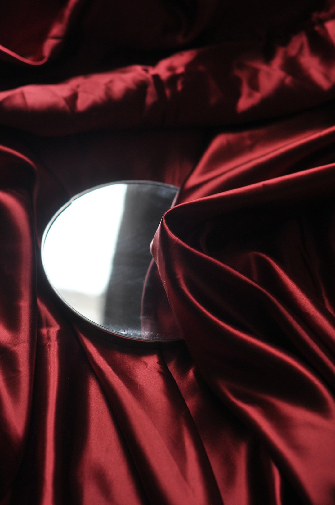 round gray framed mirror on red textile
