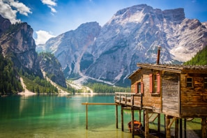 brown wooden house beside body of water overlooking rocky mountain during daytime