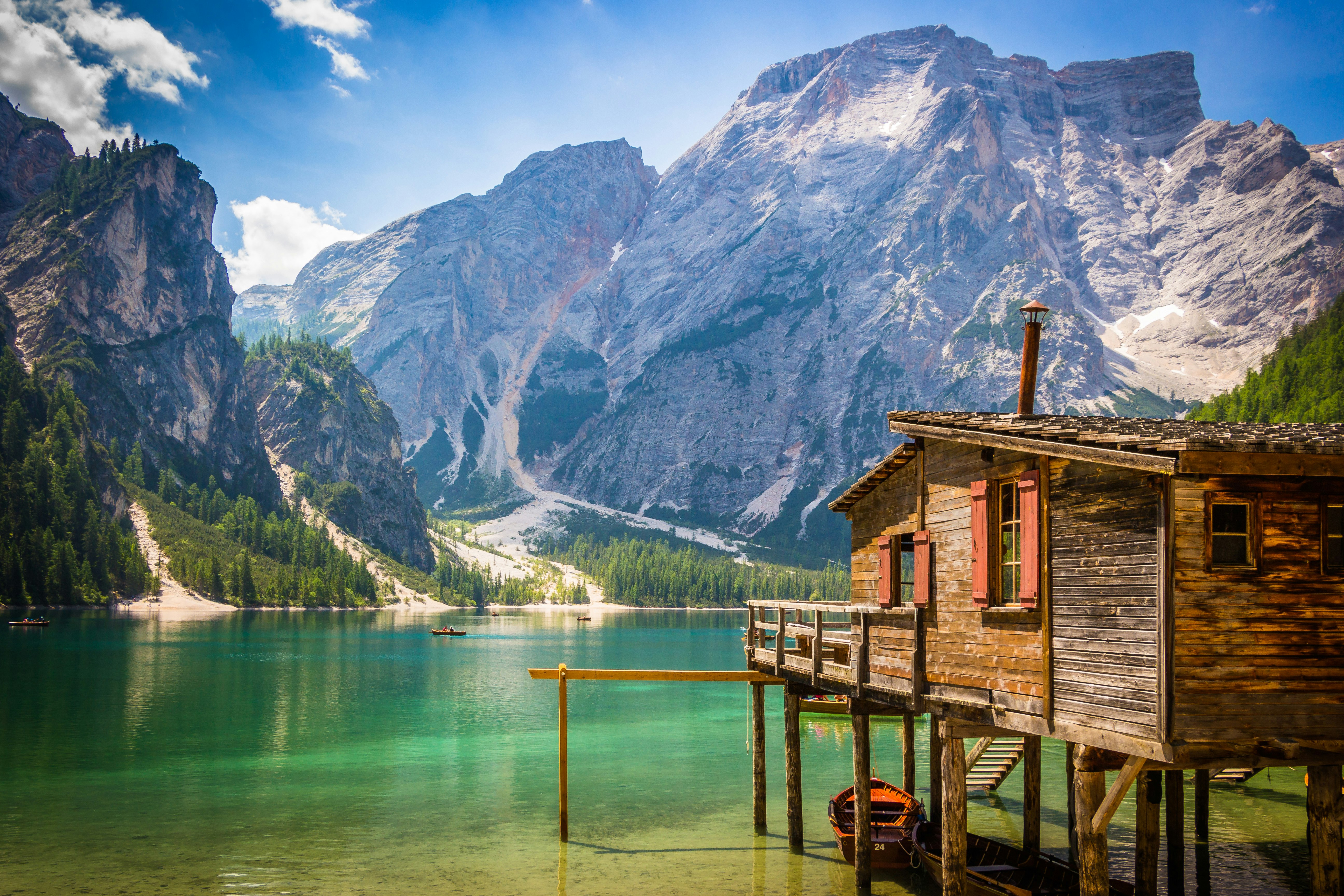 brown wooden house beside body of water overlooking rocky mountain during daytime