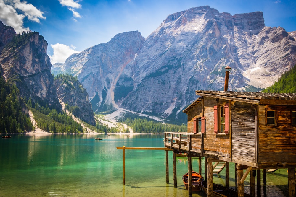 brown wooden house beside body of water overlooking rocky mountain during daytime