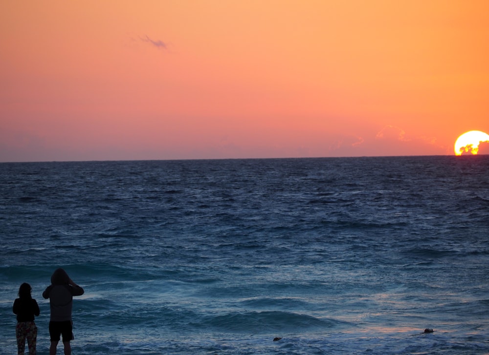 two person standing near sea during sunset