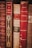 A collection of vintage books with ornate spines in various shades of red and brown. The titles and authors, such as A. France and Lamartine, are embossed in gold lettering, adding a sense of history and classic elegance to the scene.