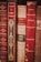 A collection of vintage books with ornate spines in various shades of red and brown. The titles and authors, such as A. France and Lamartine, are embossed in gold lettering, adding a sense of history and classic elegance to the scene.