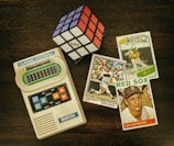 three baseball trading cards beside Rubik's cube and Classic Football handheld game console