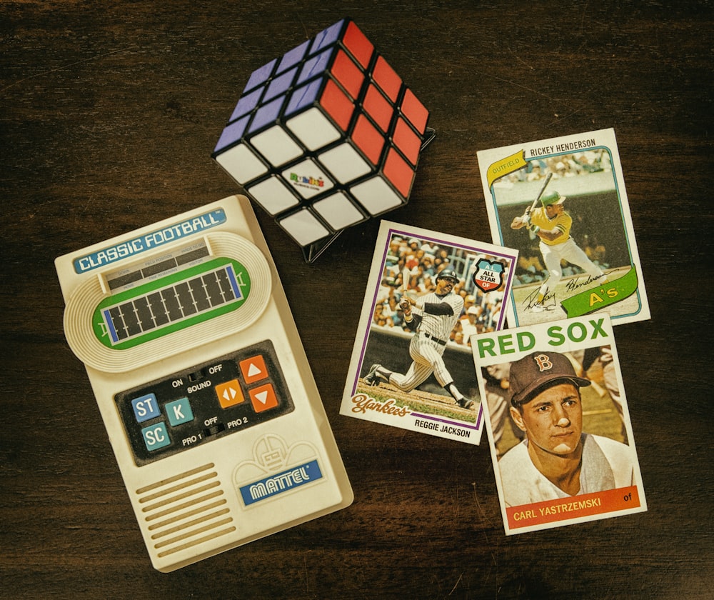 three baseball trading cards beside Rubik's cube and Classic Football handheld game console