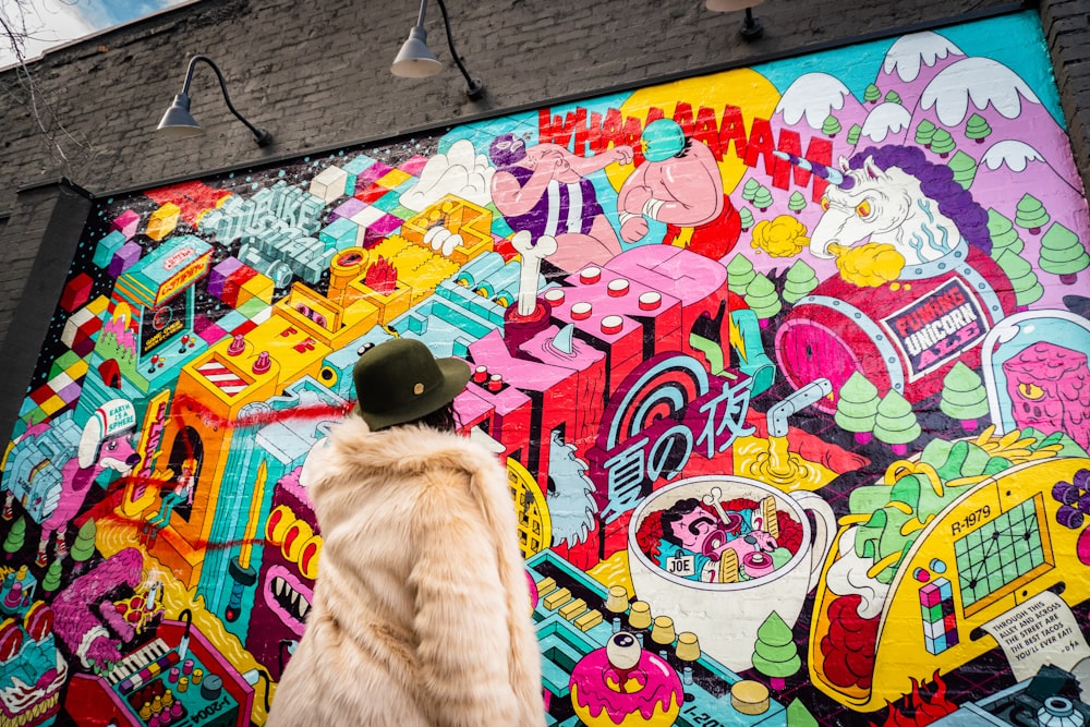 person wearing gray fur coat looking at graffiti during daytime