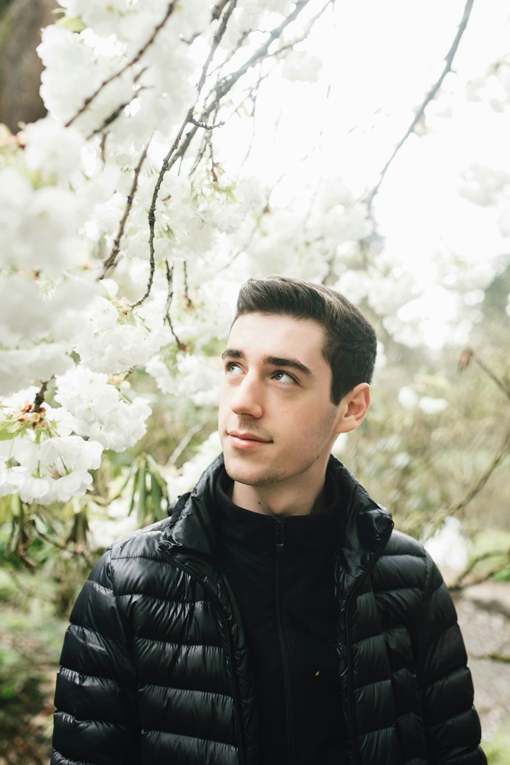 man in black bubble jacket standing under white flowering tree