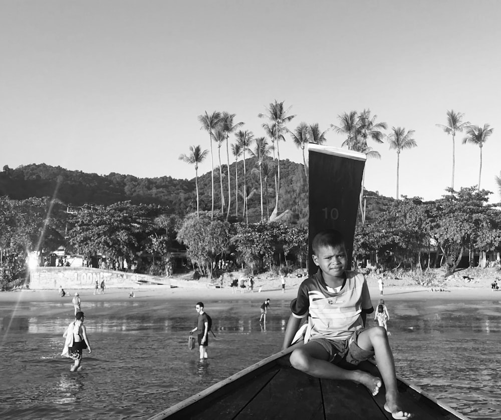 grayscale photo of boy sitting on boat