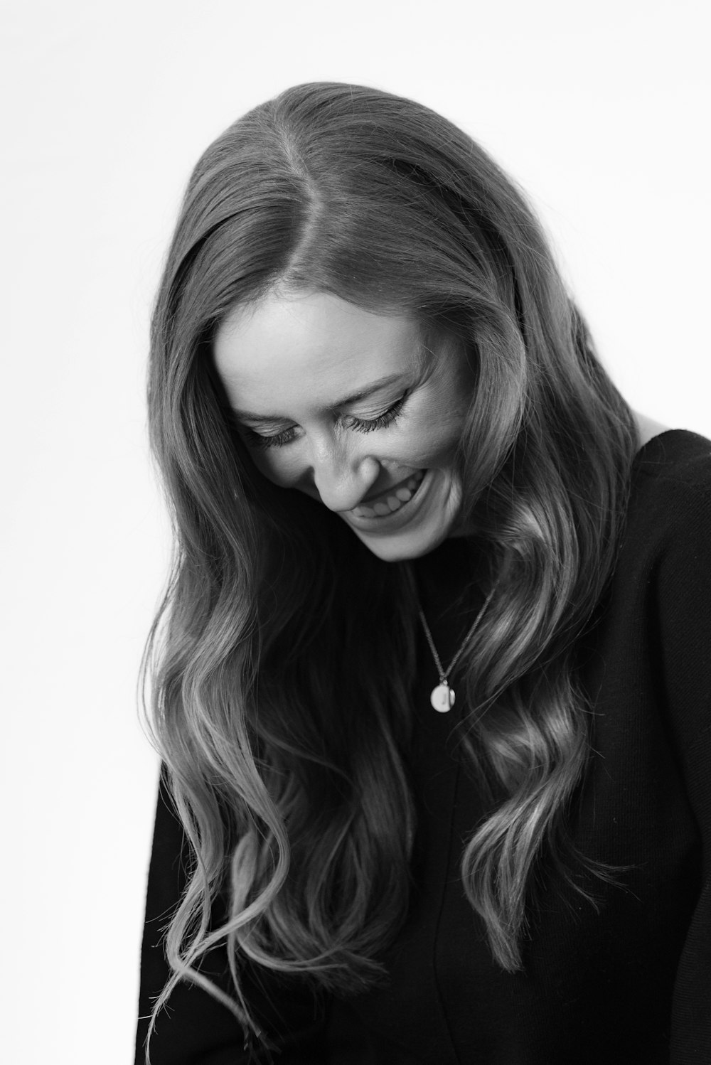 grayscale photography of smiling woman wearing black dress and pendant necklace