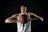 A basketball player with curly hair is wearing a white jersey with the number 12. He is holding a basketball with both hands close to his chest. The background is dark, highlighting his focused expression and muscular build.