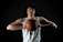 A basketball player with curly hair is wearing a white jersey with the number 12. He is holding a basketball with both hands close to his chest. The background is dark, highlighting his focused expression and muscular build.
