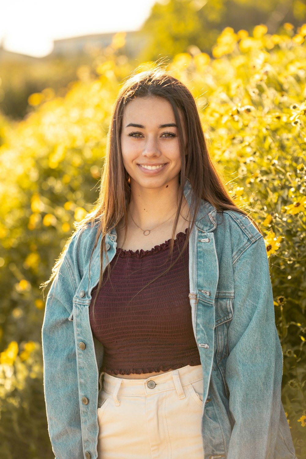 smiling woman wearing blue denim jacket near the yellow flower field during daytime